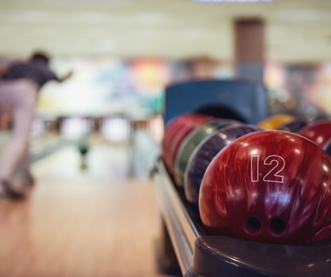 Man throwing a red bowling ball, colorful balls in the foreground